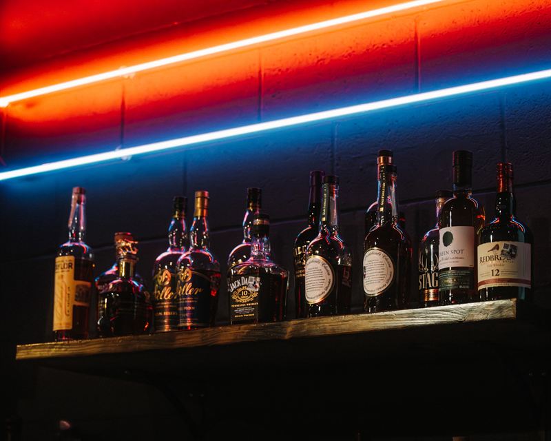 Whiskey bottles lined up on the back bar under neon lights