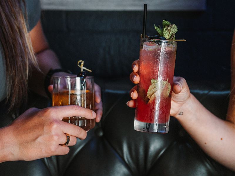 Two craft cocktails raised in a toast in a leather booth at Rodeo & Rye