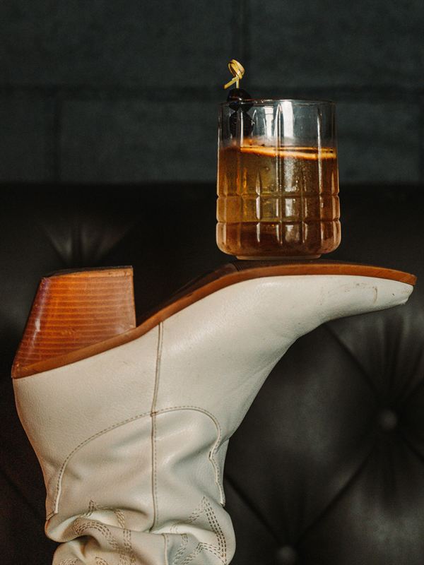 An old fashioned cocktail resting on a white cowboy boot